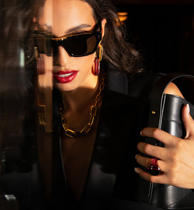 A model wearing sunglasses, gold jewerly, and red lipstick, holding the Violette black italian eather handbag from Studio DRÈA in an editorial photo shooting for Elle Arabia.