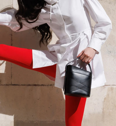 A model wearing red tights and a white chemise holding the Studio DRÈA Violette black leather handbag in a L'Officiel  editorial photo shooting