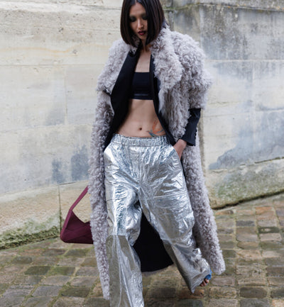 A woman wearing a shearling trench coat in grey, silver pants and heels, holding an aubergine italian leather Lulu handbag from Studio DRÈA for a L'Officiel Monaco editorial photo shooting