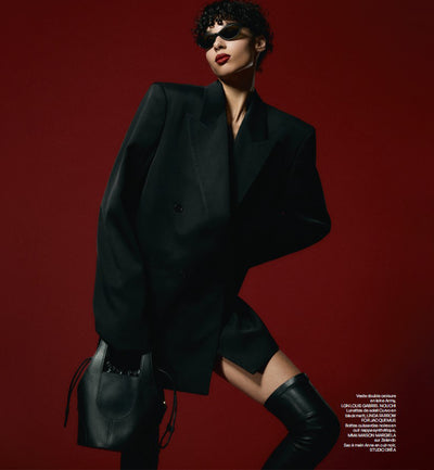 Black bucket leather handbag from Studio DRÈA featured in the Oniriq editorial with a model wearing all black against a red elegant background