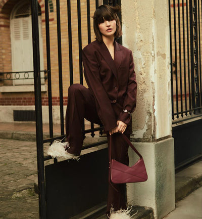 Lulu shoulder handbag from Studio DRÈA featured in an editorial shooting where a model wearing brown suit holds the bag while in front a gate in a paris scenery for june 2026 edition.
